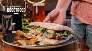 Sándwich gourmet de Sanguchería DoceTrece en Chile con camarones, hojas verdes y papas rústicas, acompañado de cerveza artesanal en mesa del restaurante