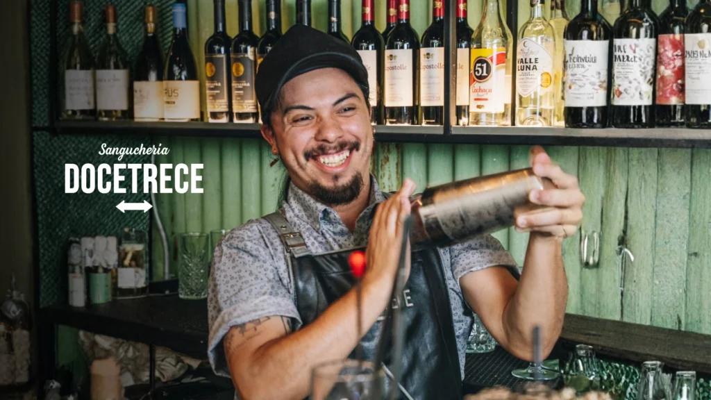 Bartender preparando destilados cóctel en la barra de Sanguchería DoceTrece en Chile, coctelería de autor con destilados y botellas en exhibición