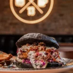 Hamburguesas artesanales gourmet de Sanguchería DoceTrece en pan negro con salsa cremosa y cebolla morada, servida en restaurante en Chile