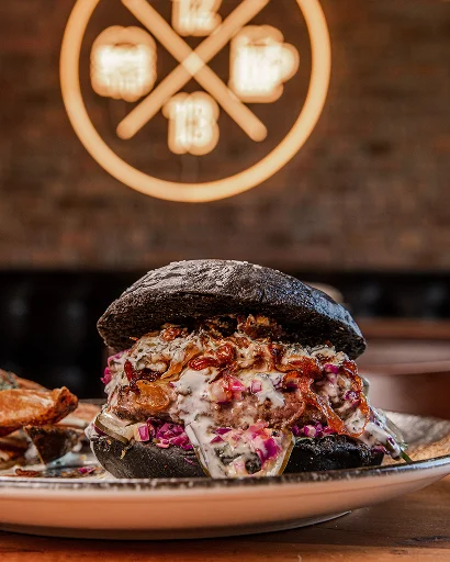Hamburguesa gourmet de Sanguchería DoceTrece en pan negro con salsa cremosa y cebolla morada, servida en restaurante en Chile