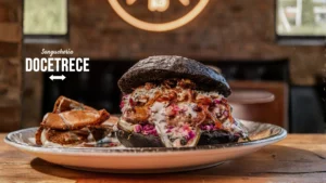 Hamburguesa gourmet de Sanguchería DoceTrece en Chile con pan negro, carne jugosa, salsa cremosa y cebolla morada, servida con papas rústicas. Blend de Carne