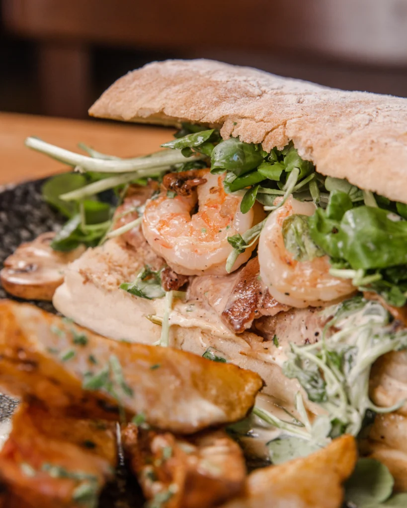 Sándwiches de atún y camarones de Sanguchería DoceTrece en Chile con hojas verdes y salsa cremosa, servido con papas rústicas artesanales