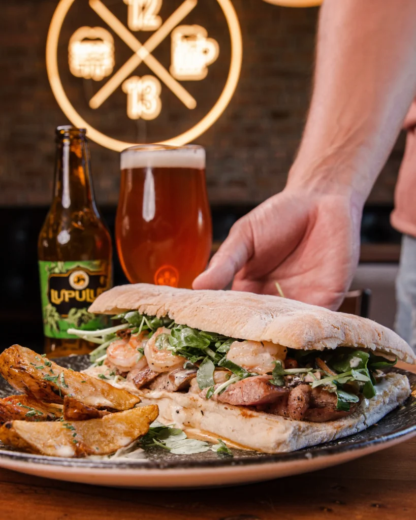 Sándwich gourmet de Sanguchería DoceTrece en Chile con camarones, hojas verdes y papas rústicas, acompañado de cerveza artesanal. Sándwiches de atún