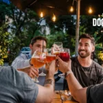 Amigos brindando con cervezas y cócteles en restobar santiago, la terraza de Sanguchería DoceTrece en Santiago de Chile, ambiente nocturno al aire libre con luces cálidas